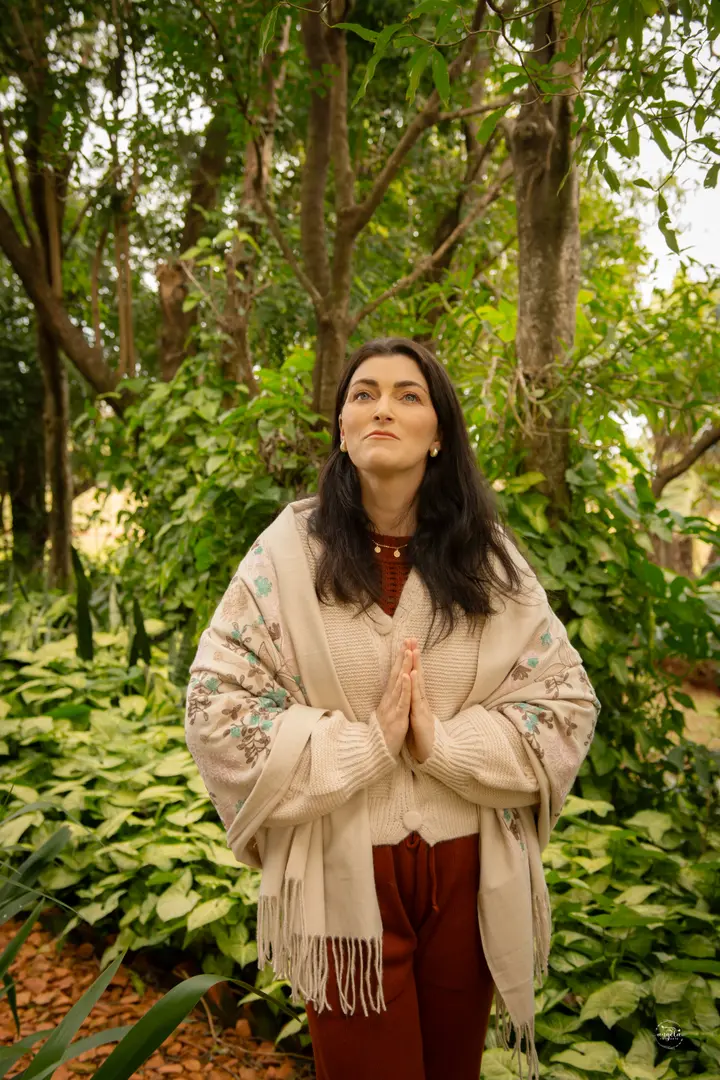 Tamitssa Tisott em meio à natureza, com um xale claro e as mãos unidas em prece